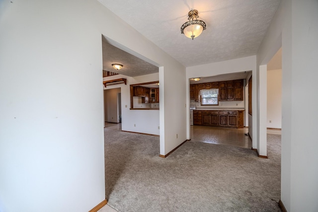 hall with baseboards, light carpet, and a textured ceiling