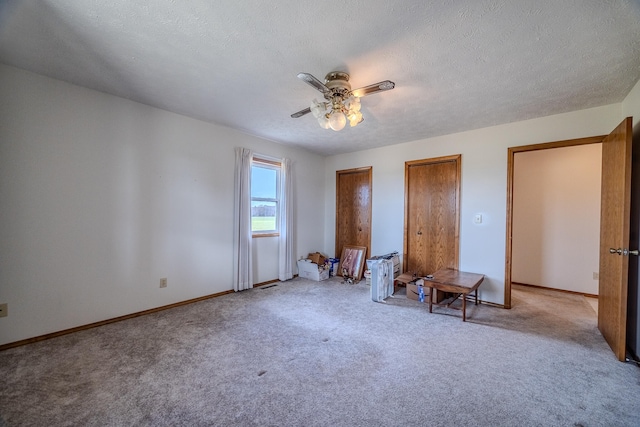 unfurnished bedroom with ceiling fan, two closets, light colored carpet, and a textured ceiling