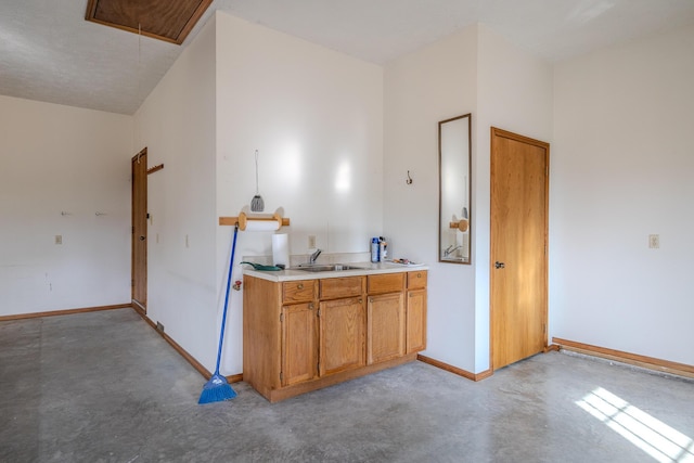 kitchen featuring concrete flooring, baseboards, light countertops, brown cabinets, and a sink