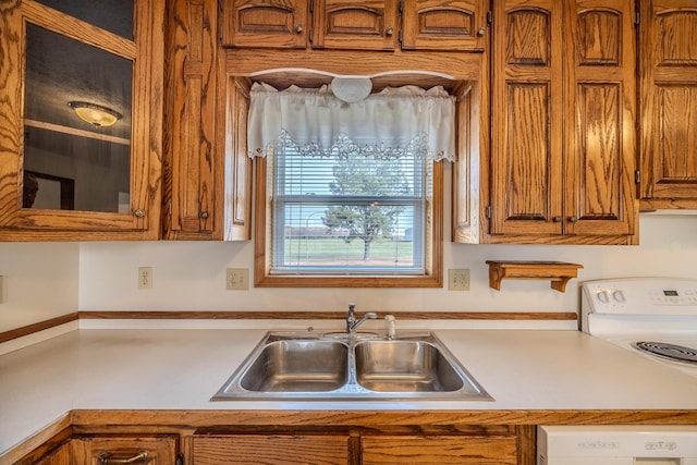 kitchen featuring a sink, light countertops, white appliances, brown cabinetry, and glass insert cabinets