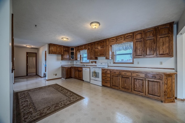 kitchen with brown cabinetry, a textured ceiling, baseboards, light floors, and white appliances