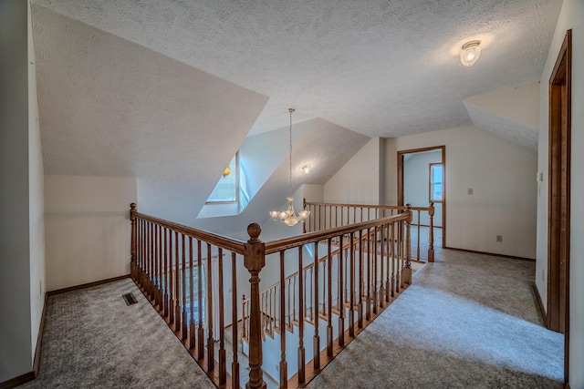 hallway featuring a notable chandelier, a textured ceiling, carpet floors, and vaulted ceiling with skylight