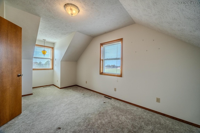 additional living space with carpet flooring, a textured ceiling, vaulted ceiling, and visible vents