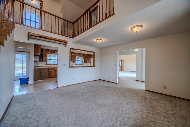 unfurnished living room featuring a towering ceiling, light carpet, and a textured ceiling