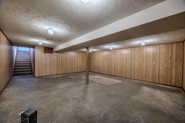 finished below grade area with stairs, wooden walls, and a textured ceiling