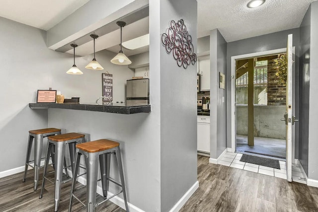 kitchen with kitchen peninsula, white cabinets, a breakfast bar area, stainless steel refrigerator, and dark hardwood / wood-style floors