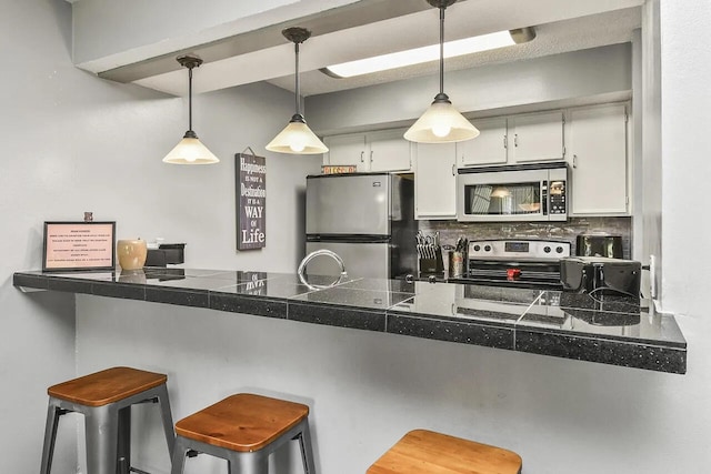 kitchen with a kitchen breakfast bar, backsplash, white cabinets, decorative light fixtures, and appliances with stainless steel finishes