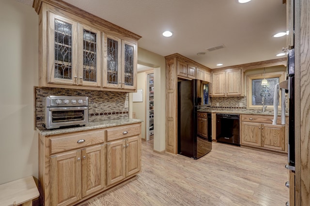 kitchen with light stone countertops, black appliances, decorative backsplash, and light hardwood / wood-style floors