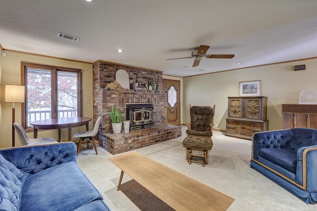 living room featuring ceiling fan, crown molding, a wood stove, and light colored carpet