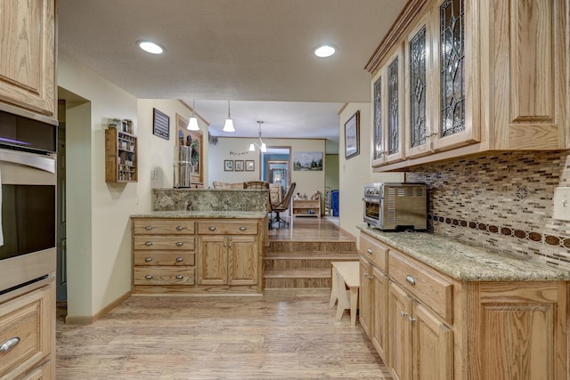 kitchen with light stone countertops, oven, backsplash, hanging light fixtures, and light hardwood / wood-style flooring