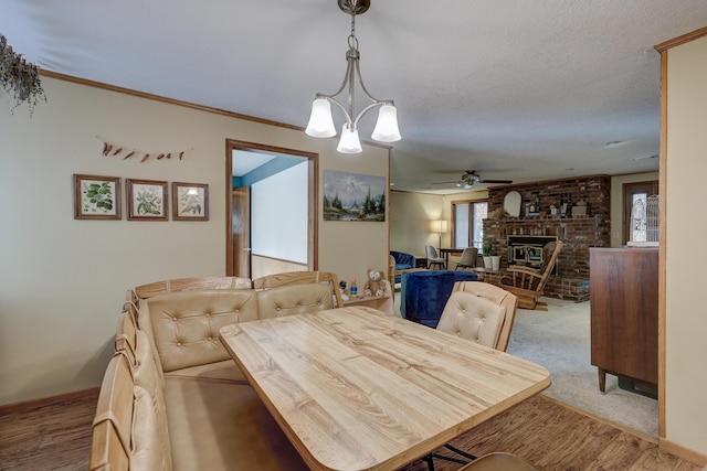 dining room featuring ceiling fan with notable chandelier, a textured ceiling, a brick fireplace, ornamental molding, and light colored carpet