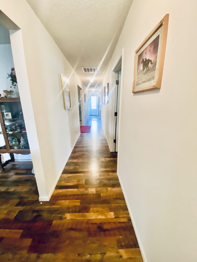hall featuring baseboards, wood finished floors, and visible vents