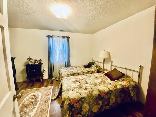 bedroom with visible vents, a textured ceiling, and wood finished floors