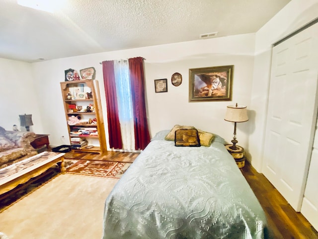 bedroom with a textured ceiling, dark hardwood / wood-style floors, and a closet