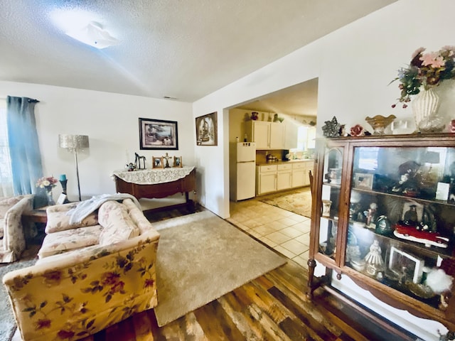 bedroom featuring multiple windows, freestanding refrigerator, light wood-type flooring, and a textured ceiling