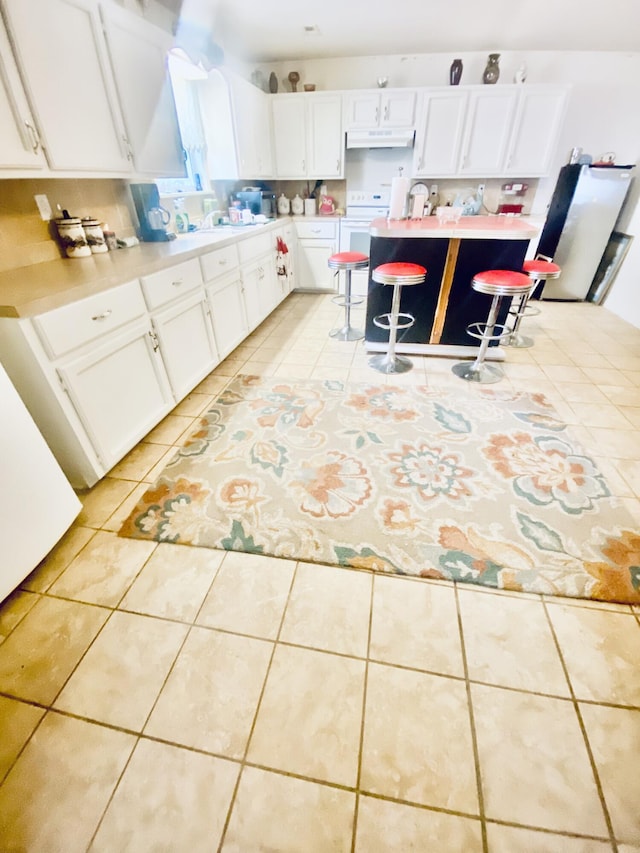 kitchen with light tile patterned flooring, light countertops, white cabinetry, a kitchen bar, and under cabinet range hood