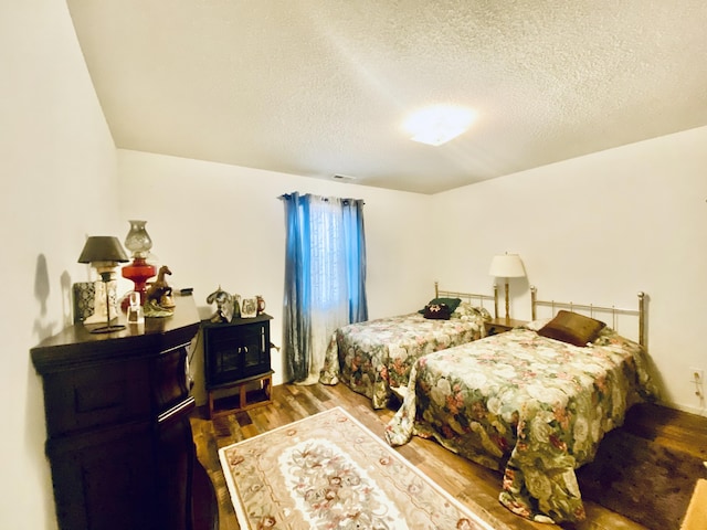 bedroom featuring a textured ceiling, a wood stove, wood finished floors, and visible vents