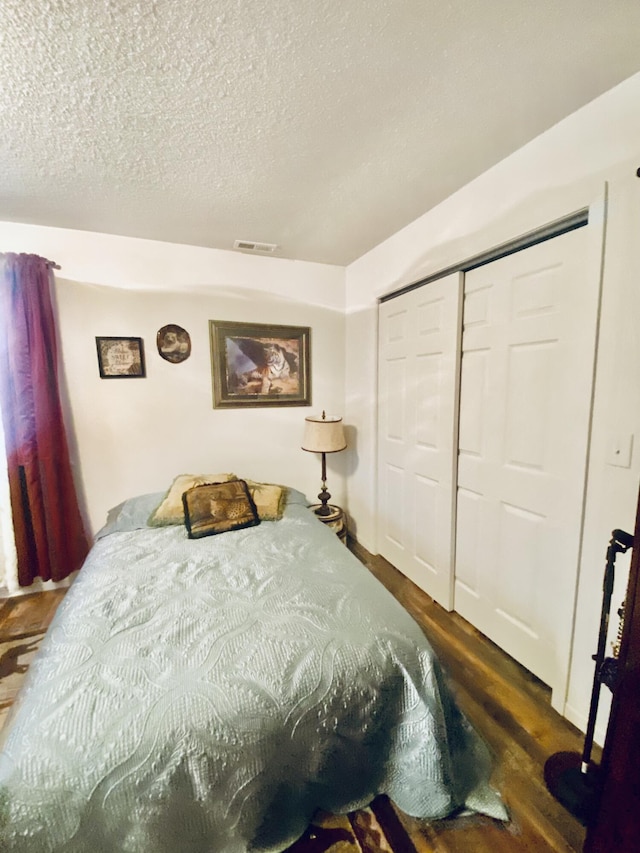 bedroom with a textured ceiling, a closet, wood finished floors, and visible vents