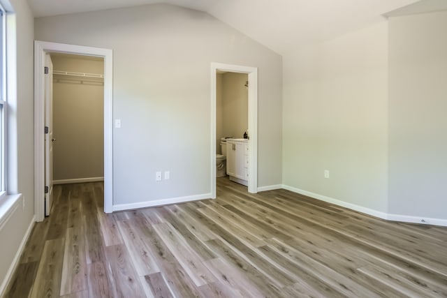 unfurnished bedroom with a walk in closet, a closet, light hardwood / wood-style floors, lofted ceiling, and connected bathroom