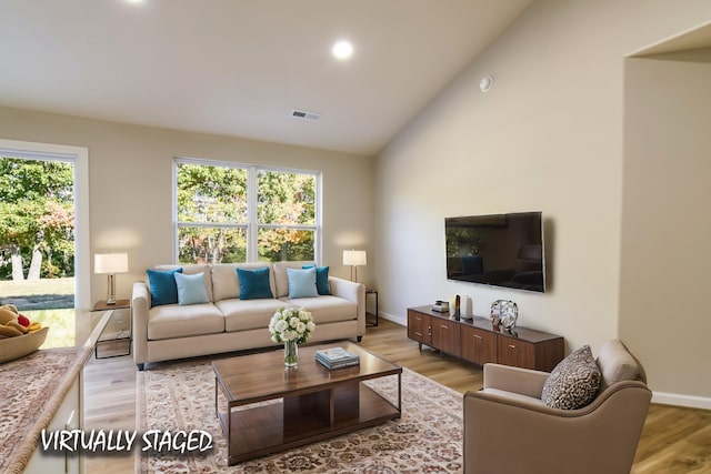 living room with a wealth of natural light, light hardwood / wood-style flooring, and high vaulted ceiling