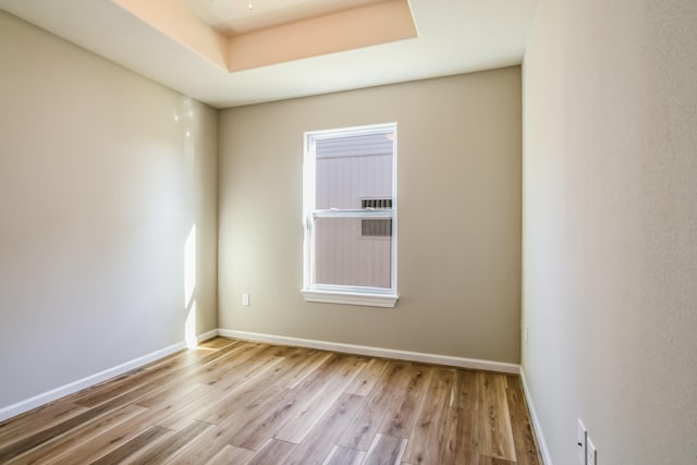 unfurnished room with light wood-type flooring and a raised ceiling