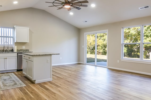 kitchen with vaulted ceiling, white cabinets, light stone counters, and light wood-type flooring