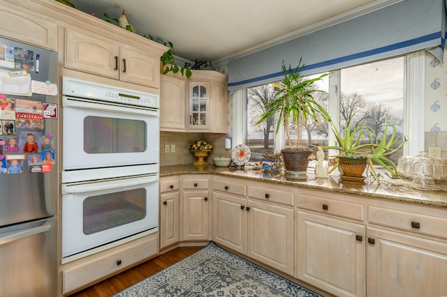 kitchen with light stone countertops, light wood-type flooring, backsplash, double oven, and stainless steel refrigerator