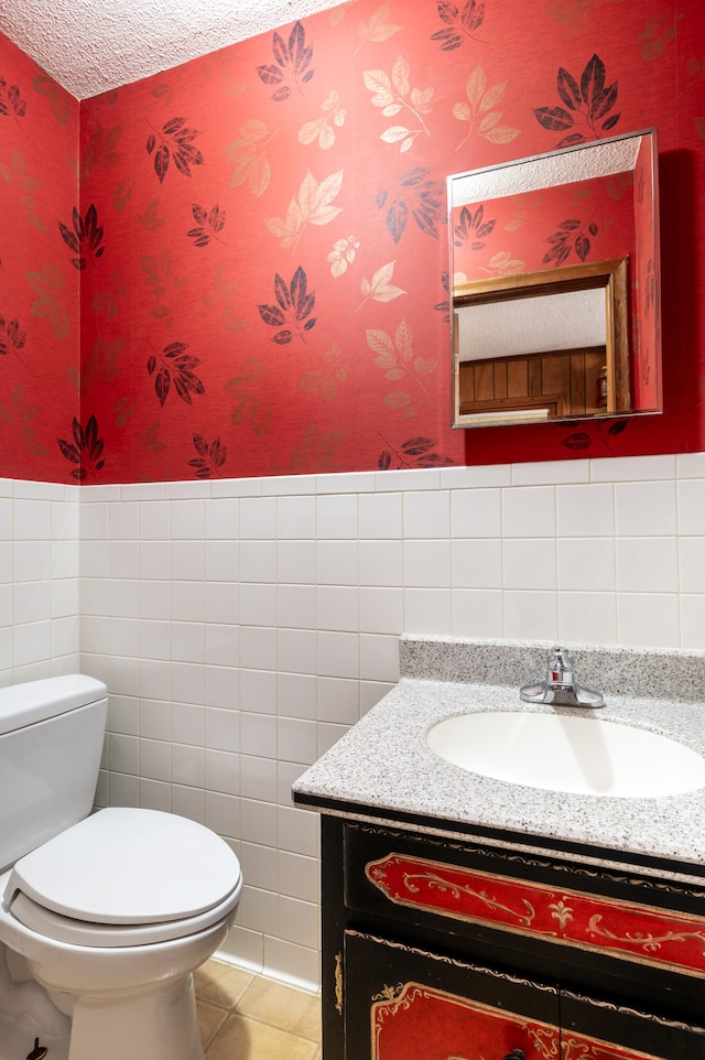 bathroom featuring tile patterned floors, toilet, vanity, tile walls, and a textured ceiling