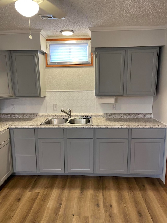 kitchen featuring ornamental molding, a textured ceiling, sink, wood-type flooring, and gray cabinets