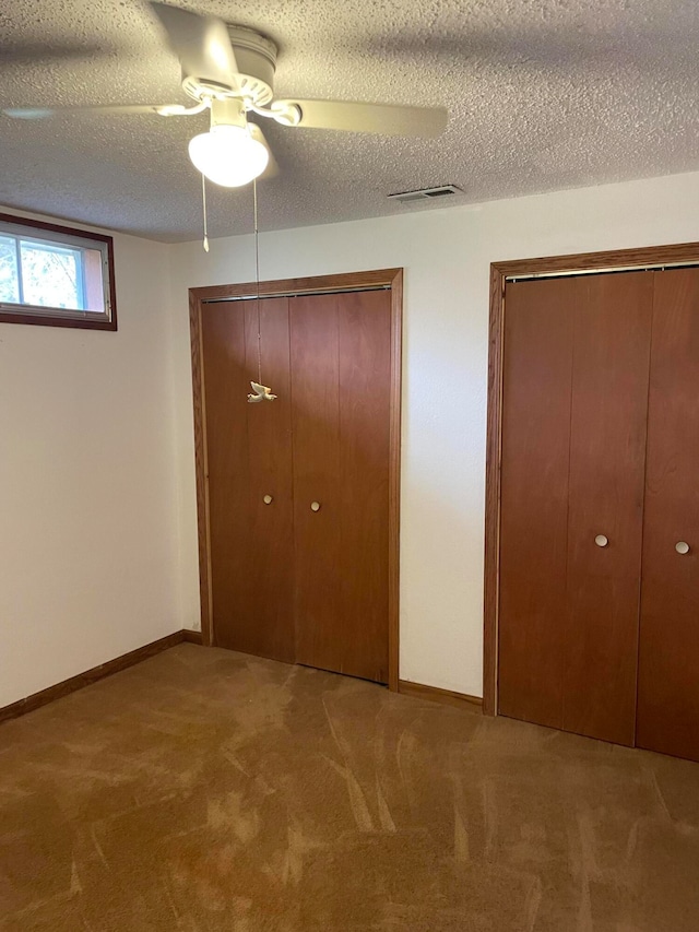 unfurnished bedroom featuring multiple closets, ceiling fan, carpet, and a textured ceiling