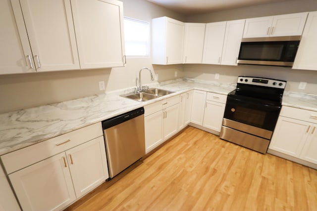 kitchen featuring light stone countertops, appliances with stainless steel finishes, sink, white cabinets, and light hardwood / wood-style flooring