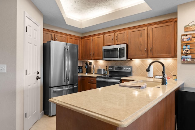 kitchen with kitchen peninsula, tasteful backsplash, a tray ceiling, sink, and stainless steel appliances