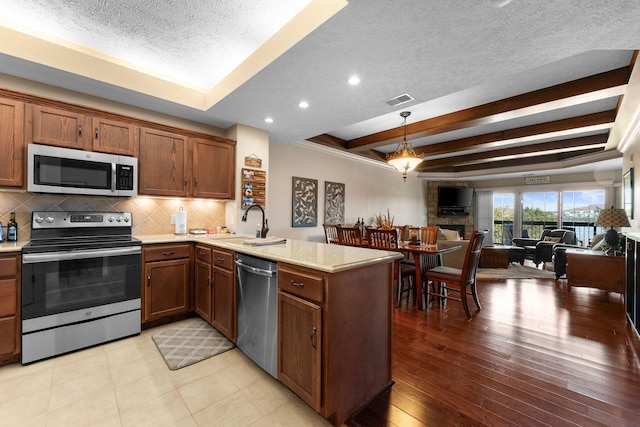 kitchen with kitchen peninsula, decorative backsplash, appliances with stainless steel finishes, beamed ceiling, and light hardwood / wood-style floors