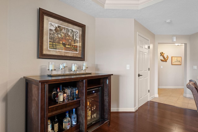 bar featuring wine cooler, a textured ceiling, and hardwood / wood-style flooring