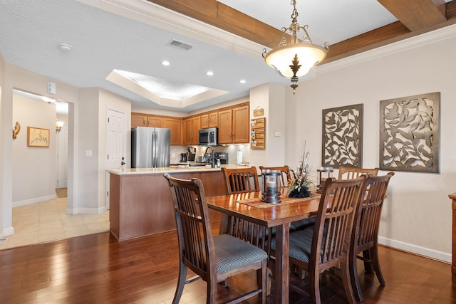 dining space with a raised ceiling, a textured ceiling, and light hardwood / wood-style flooring