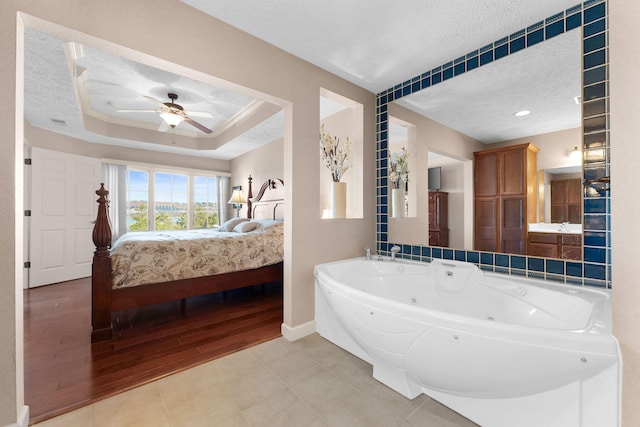 bathroom with hardwood / wood-style floors, ceiling fan, a raised ceiling, a textured ceiling, and a bath