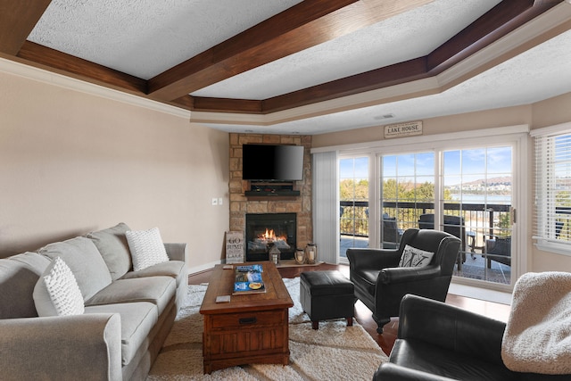 living room featuring a stone fireplace, a textured ceiling, and a tray ceiling