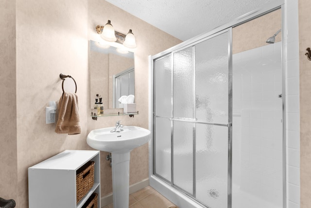 bathroom featuring a shower with door, a textured ceiling, sink, and tile patterned flooring