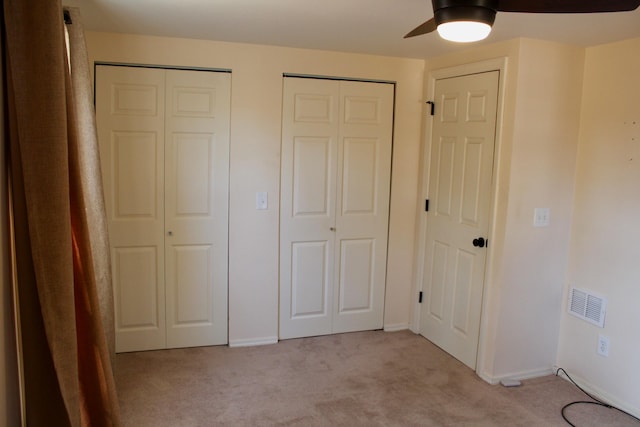 unfurnished bedroom with light carpet, multiple closets, and ceiling fan