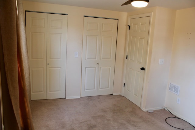 unfurnished bedroom with light carpet, multiple closets, and ceiling fan