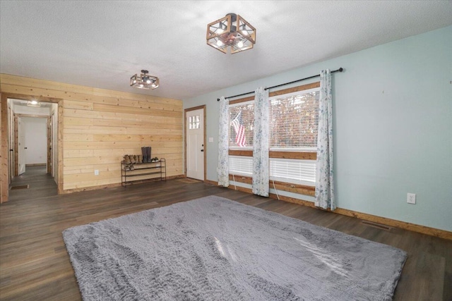 unfurnished living room with wood walls, dark hardwood / wood-style floors, a textured ceiling, and a wood stove