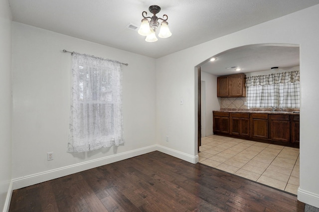 unfurnished dining area with sink, a notable chandelier, a textured ceiling, and light wood-type flooring