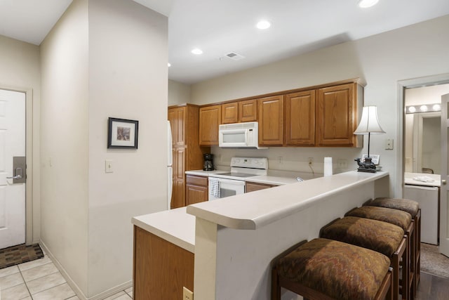 kitchen with white appliances, light tile patterned floors, kitchen peninsula, and a kitchen breakfast bar