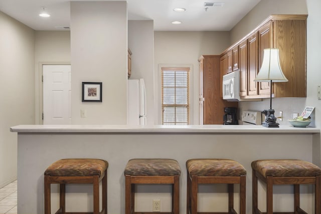 kitchen with kitchen peninsula, light tile patterned floors, a breakfast bar, and white appliances