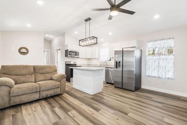 kitchen featuring appliances with stainless steel finishes, hanging light fixtures, white cabinetry, light hardwood / wood-style floors, and vaulted ceiling