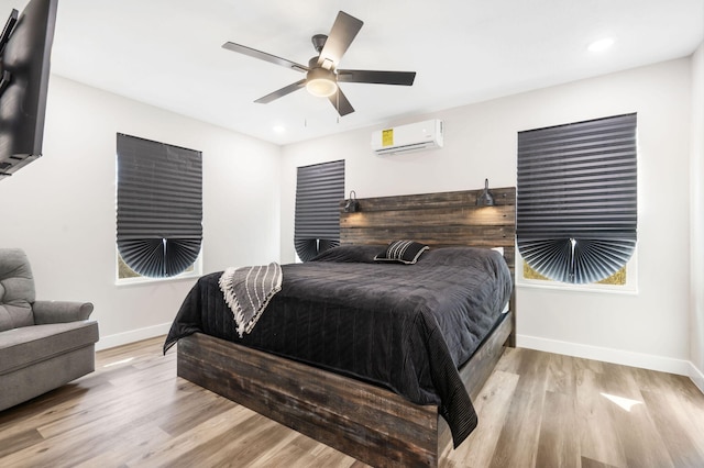 bedroom featuring ceiling fan, multiple windows, light hardwood / wood-style flooring, and a wall unit AC