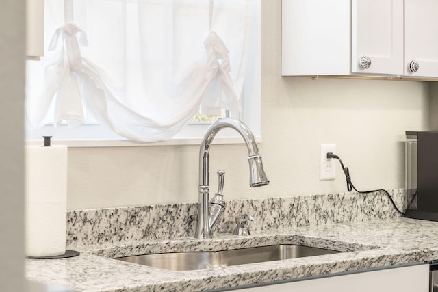 interior details with white cabinets, sink, and light stone counters