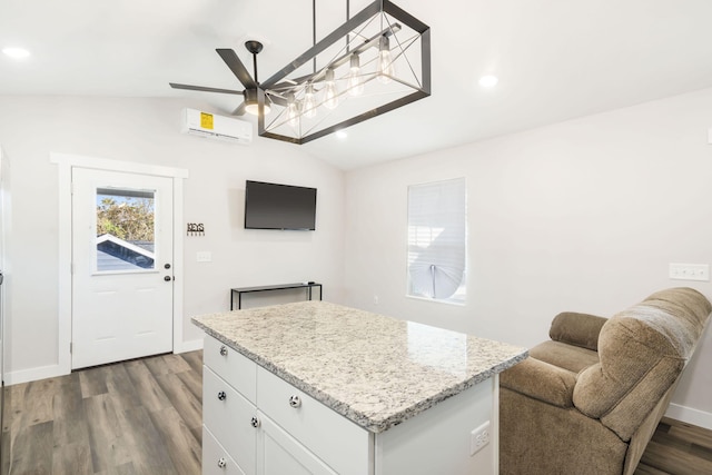 kitchen featuring lofted ceiling, white cabinets, hardwood / wood-style floors, light stone countertops, and a wall mounted air conditioner