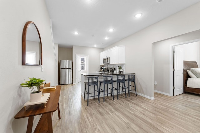 kitchen featuring white cabinets, appliances with stainless steel finishes, a kitchen bar, light wood-type flooring, and sink