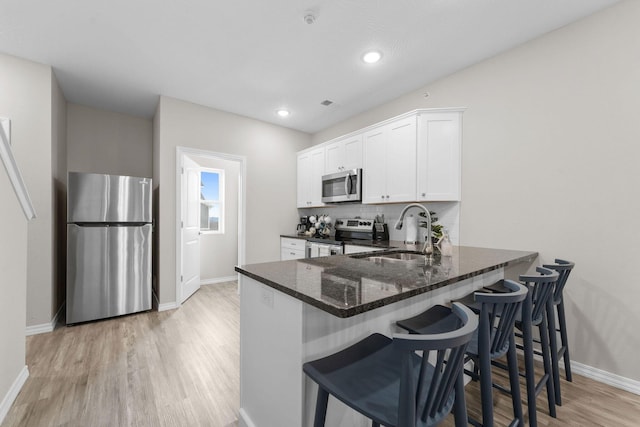 kitchen with sink, stainless steel appliances, dark stone counters, white cabinets, and light hardwood / wood-style flooring